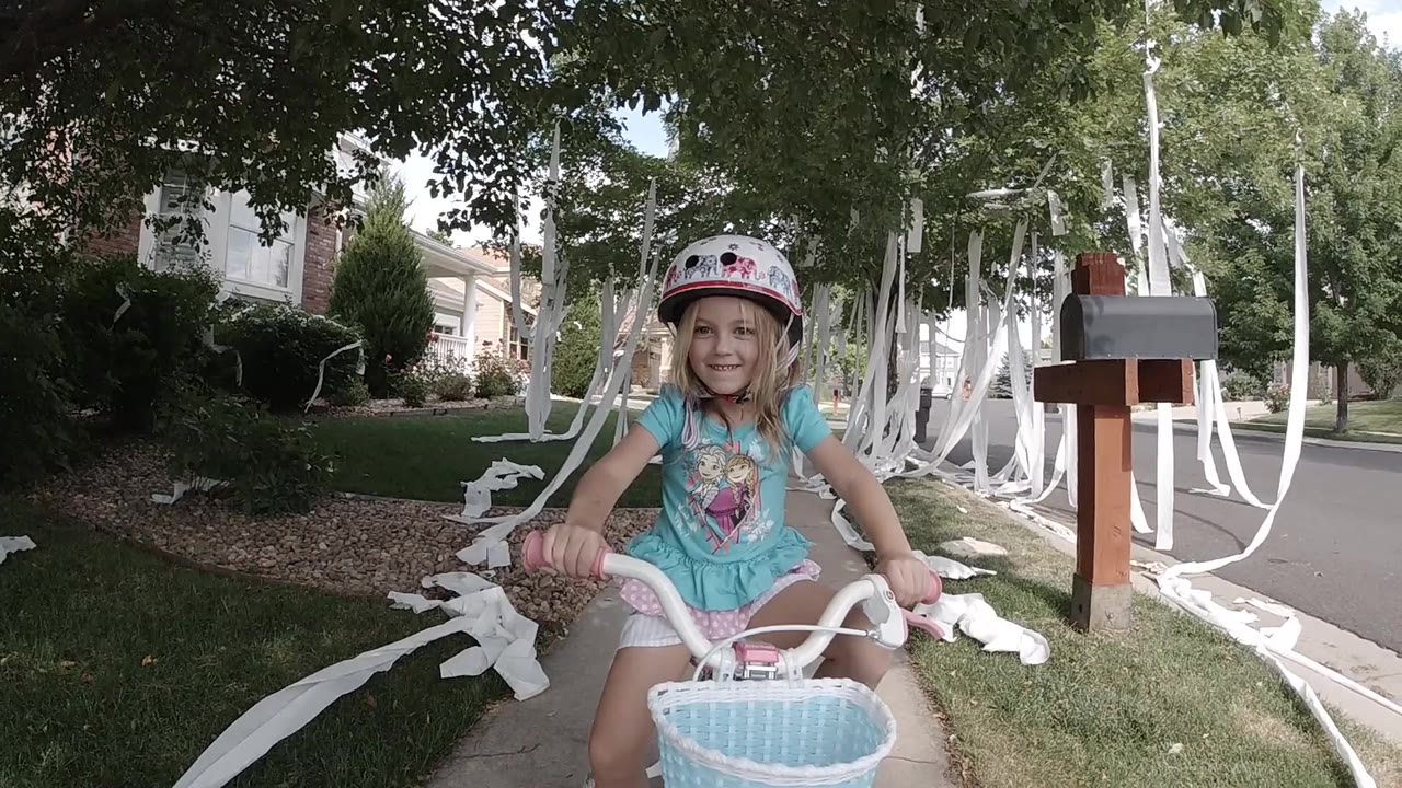A young girl in a helmet smiles on a small white bicycle in Colorado, with white streamers, grass, mailboxes, and houses behind her.