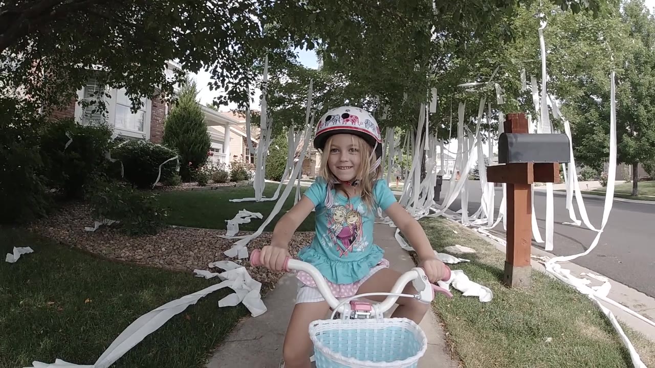 Helmeted girl on bicycle smiles in front of streamers on a sidewalk.