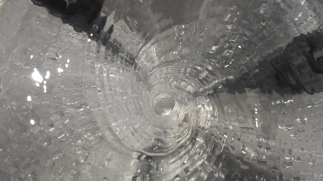 Overhead Denver clip frame showing clear water circling the centered toilet bowl drain before any ball appears, with no visible people.