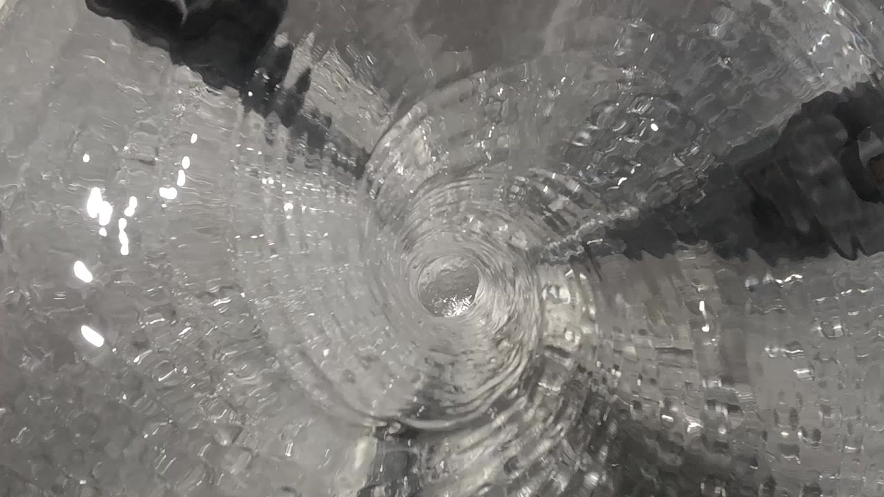 Clear toilet water spins around the central drain with bright surface reflections and no ball in view, no visible people.