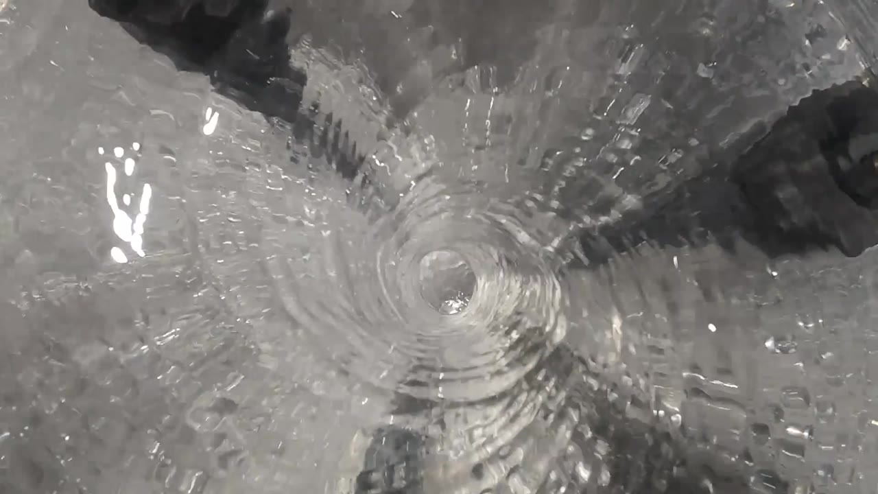 Reflective water swirls toward a toilet bowl drain.