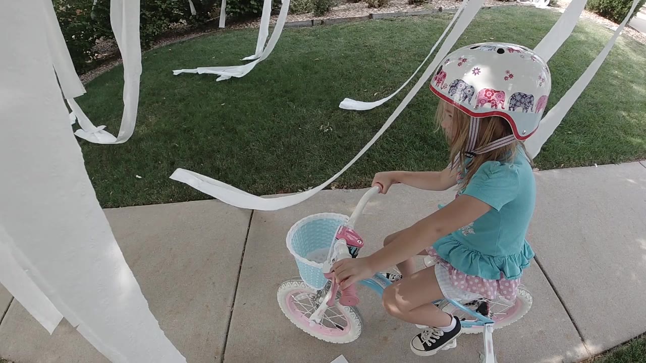 Girl in a helmet on a small bicycle under white streamers.