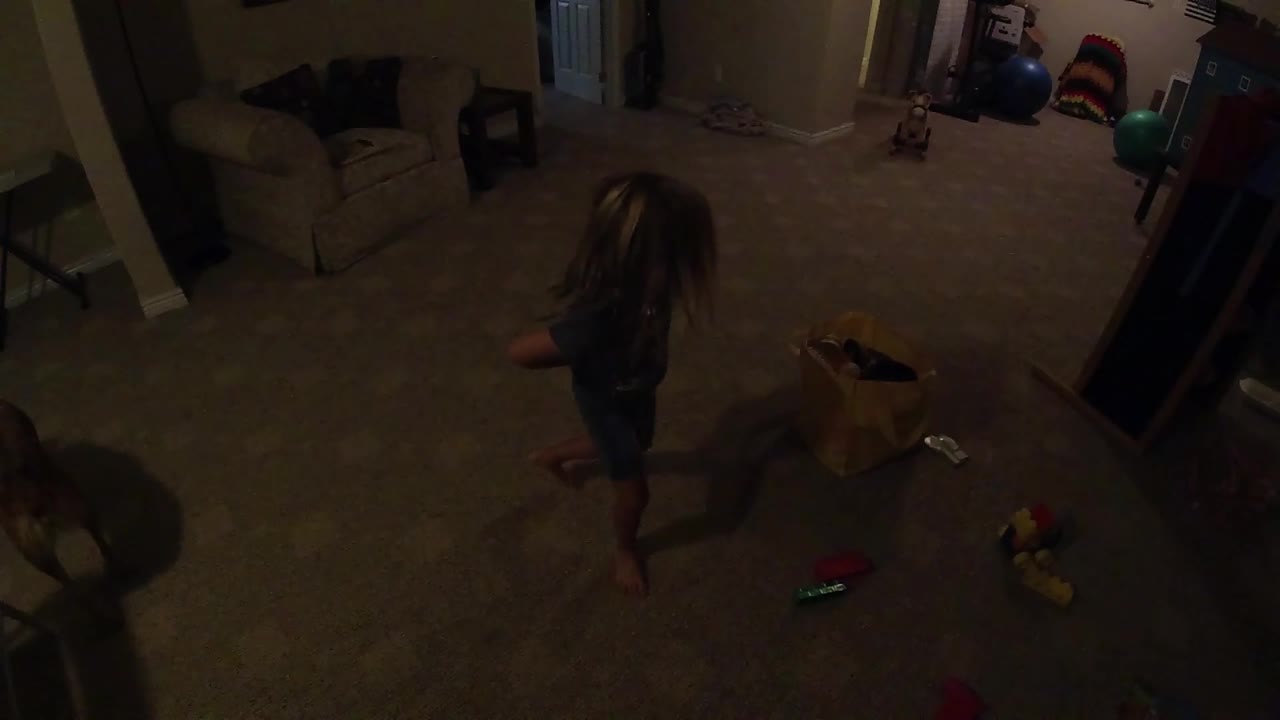 The girl begins moving away from the yellow bag across the open carpet while toys and storage remain visible in the background.
