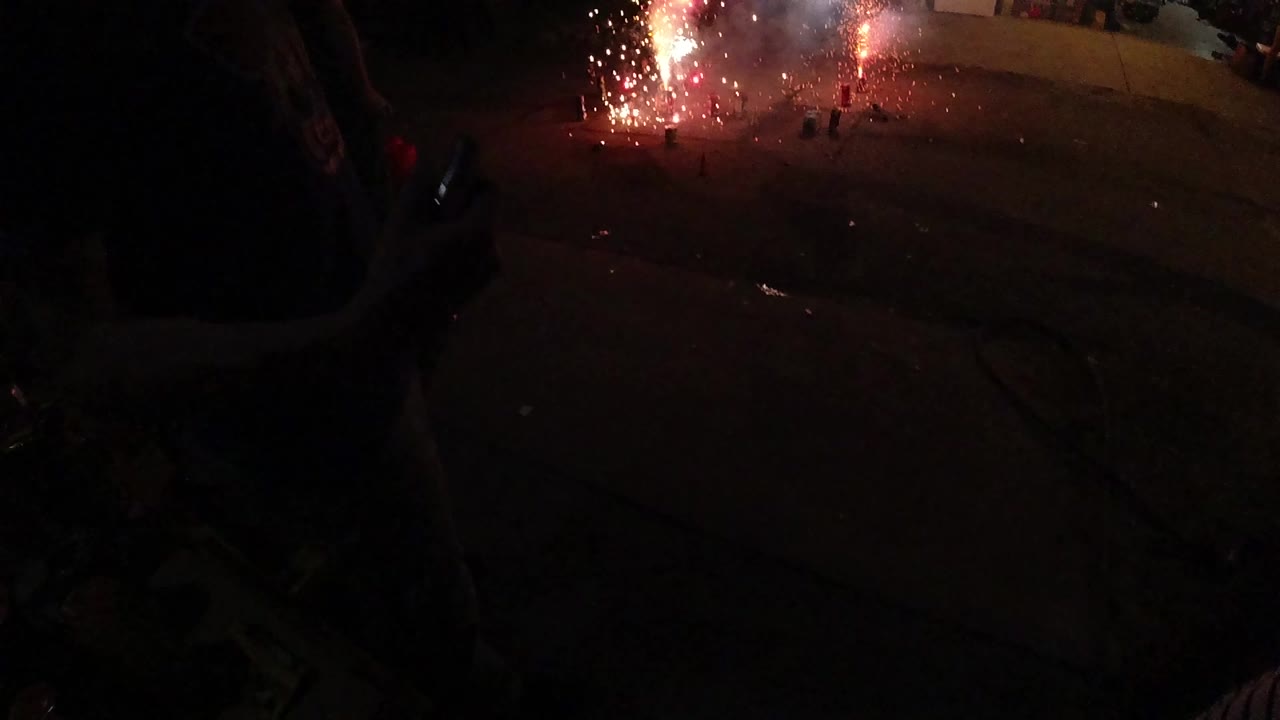 Bright sparks and smoke rise from fireworks on pavement.