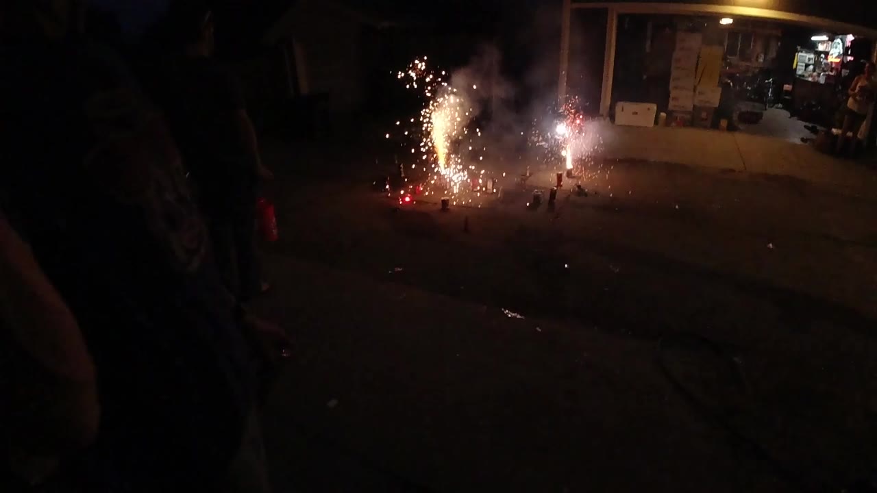 Fireworks spark on pavement with smoke in front of a garage.