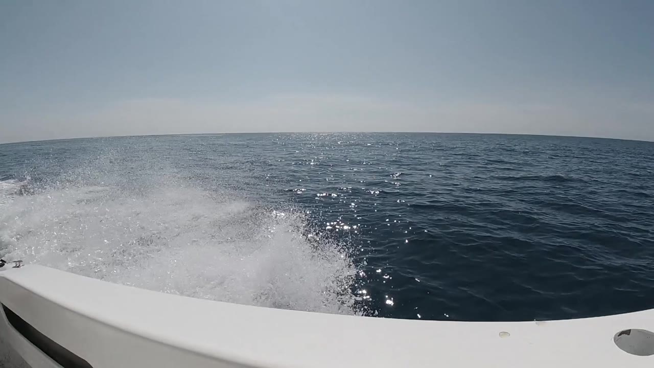 The boat wake breaks into white spray at left while sun flecks scatter across the darker water beyond, with no visible people.