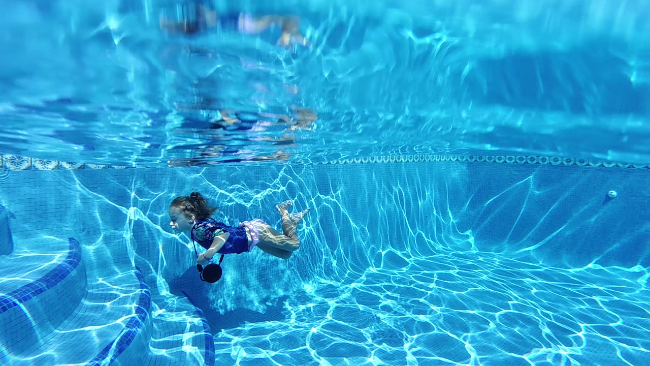 Child underwater near a pool wall and surface line.
