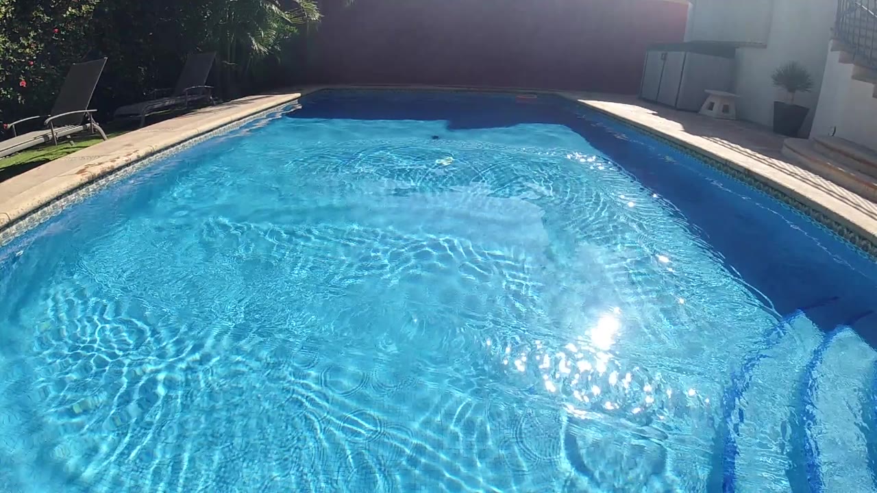 Outdoor swimming pool from above, vivid blue water, sun reflection on surface, pool coping and steps at lower left