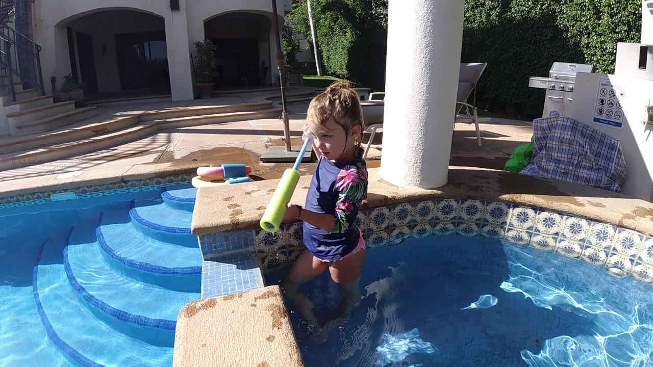 Child in pool lifting a green toy near the ledge.