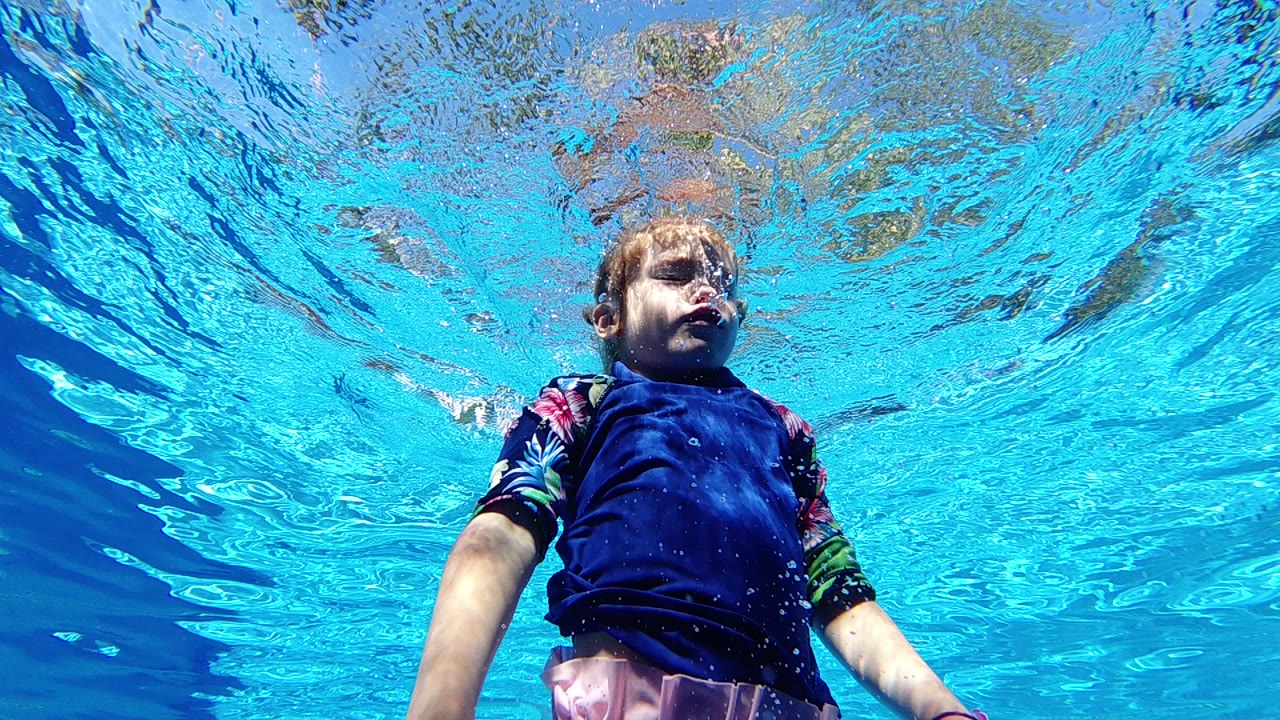 Young child underwater in a blue swim top near the pool surface.