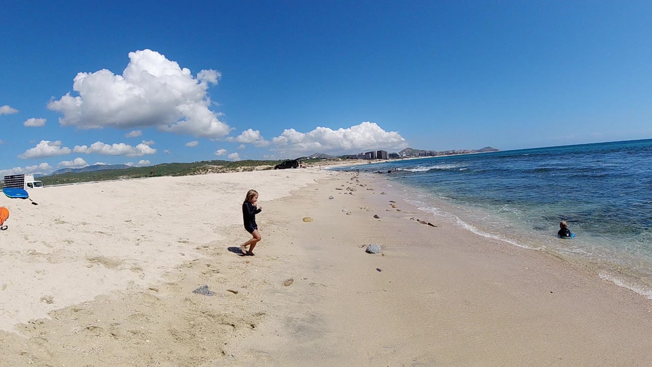 Wide beach view with a child walking near the shoreline and another child in shallow water.