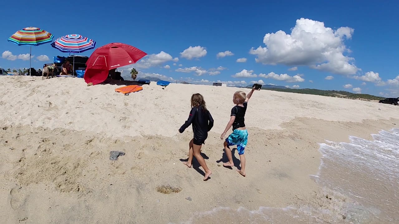Two children near foamy water and beach umbrellas