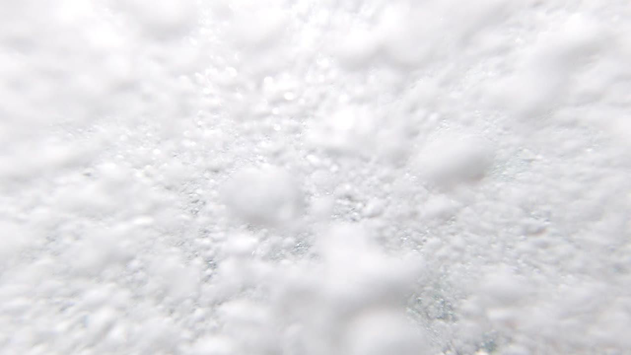 Close-up of white seafoam at the ocean surface at Los Cabos, Mexico, teal-gray water visible in small gaps between bubble clusters; no people visible