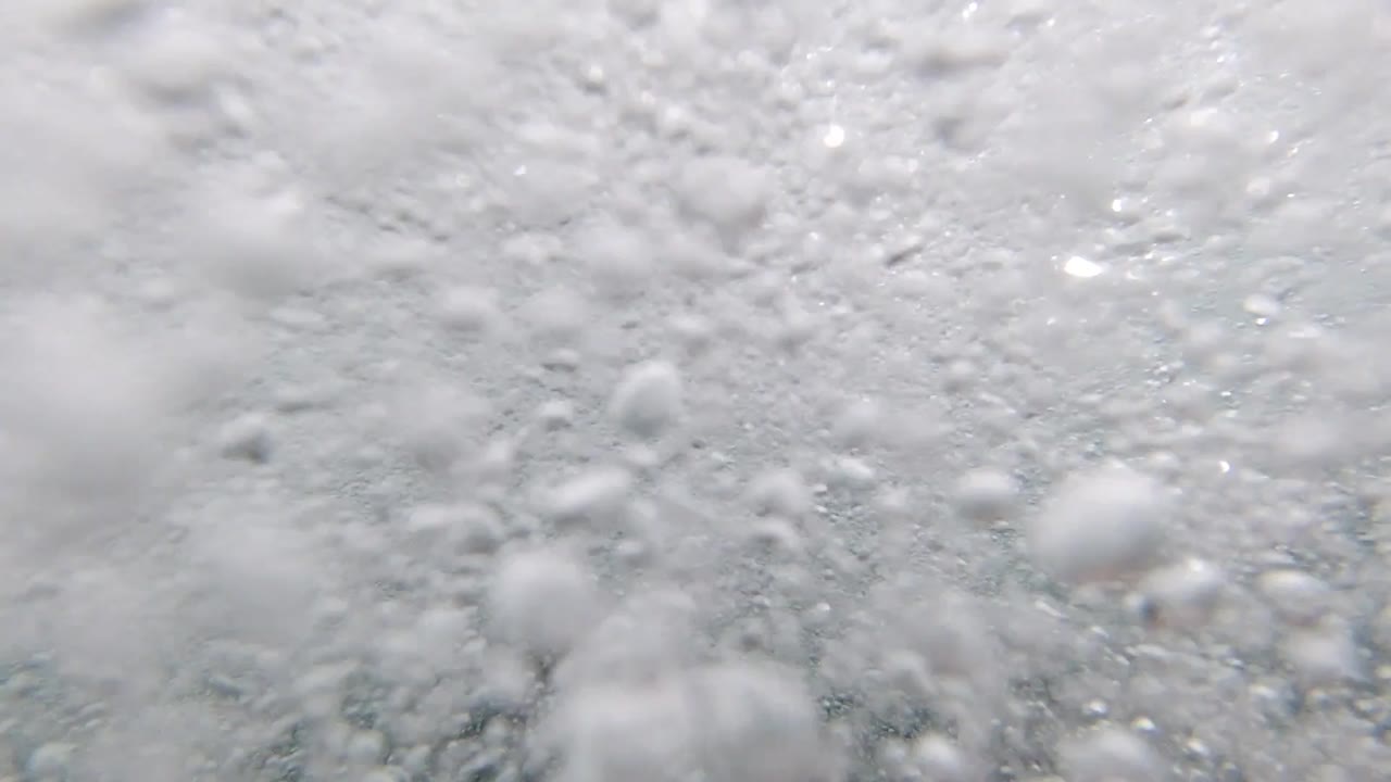 White seafoam with a larger visible patch of teal-gray water in the lower center of the frame