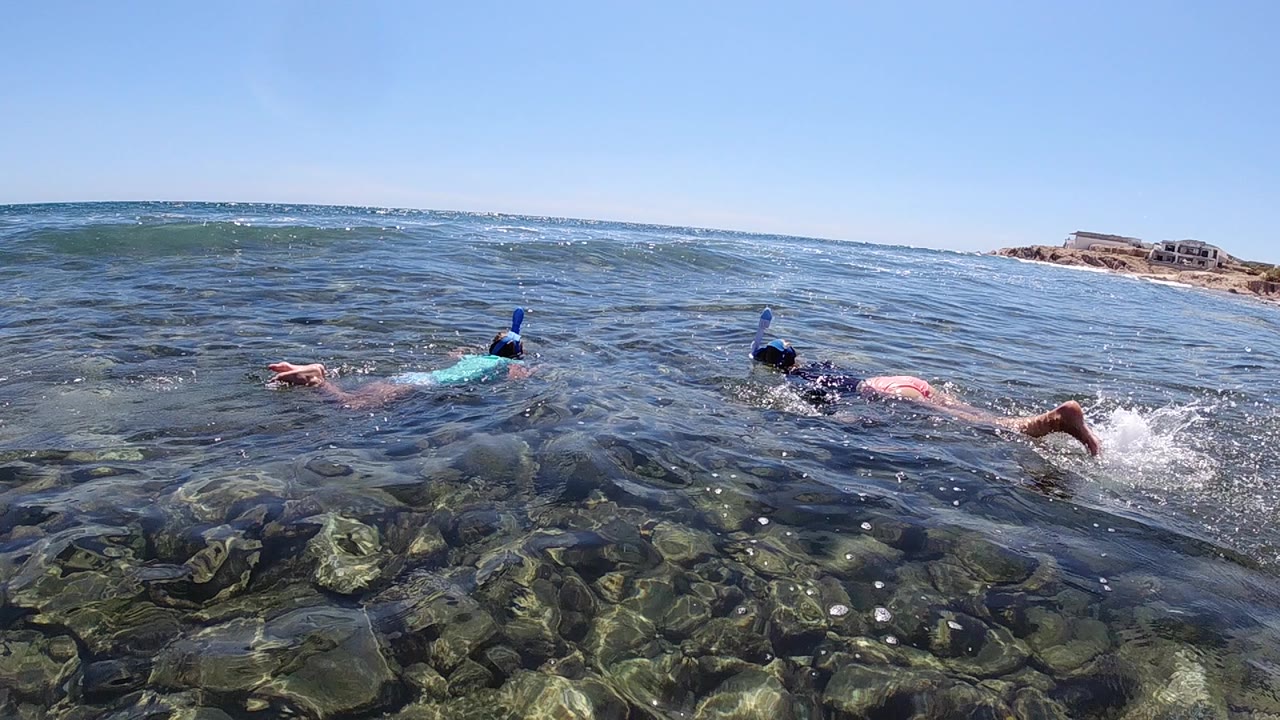 The pair of snorkelers continue swimming across shallow Los Cabos water as small surface ripples pass over the visible rock bed.
