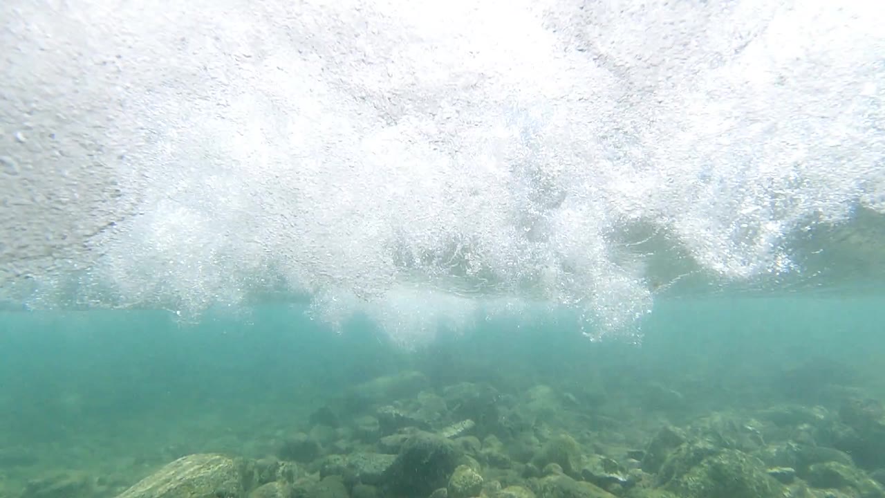 Breaking wave photographed at water level off Los Cabos, Mexico, showing dense white foam and spray over teal-green ocean water; no visible people
