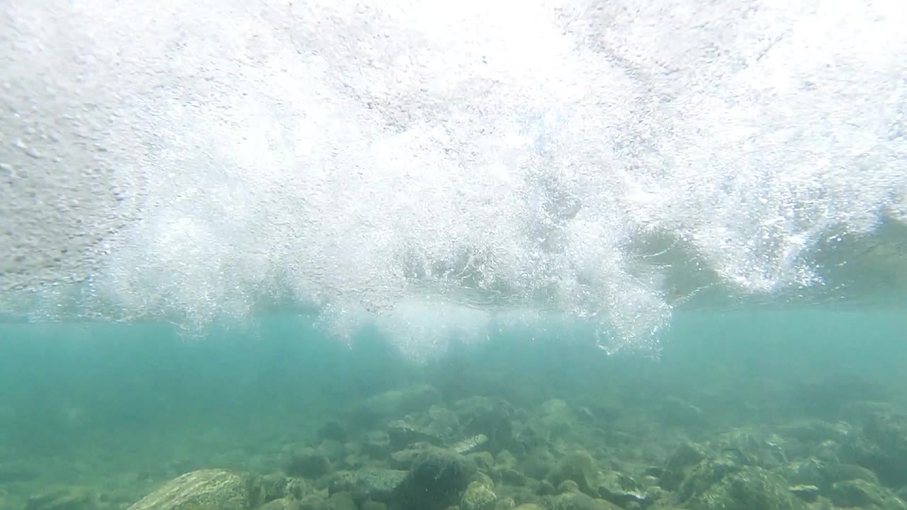 Breaking wave turbulence off Los Cabos, dense white foam filling the upper frame and teal ocean water visible below; no visible people