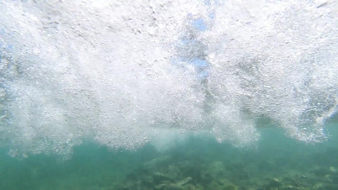 Wave foam breaking near dark rocks or reef at the waterline off Los Cabos; no visible people