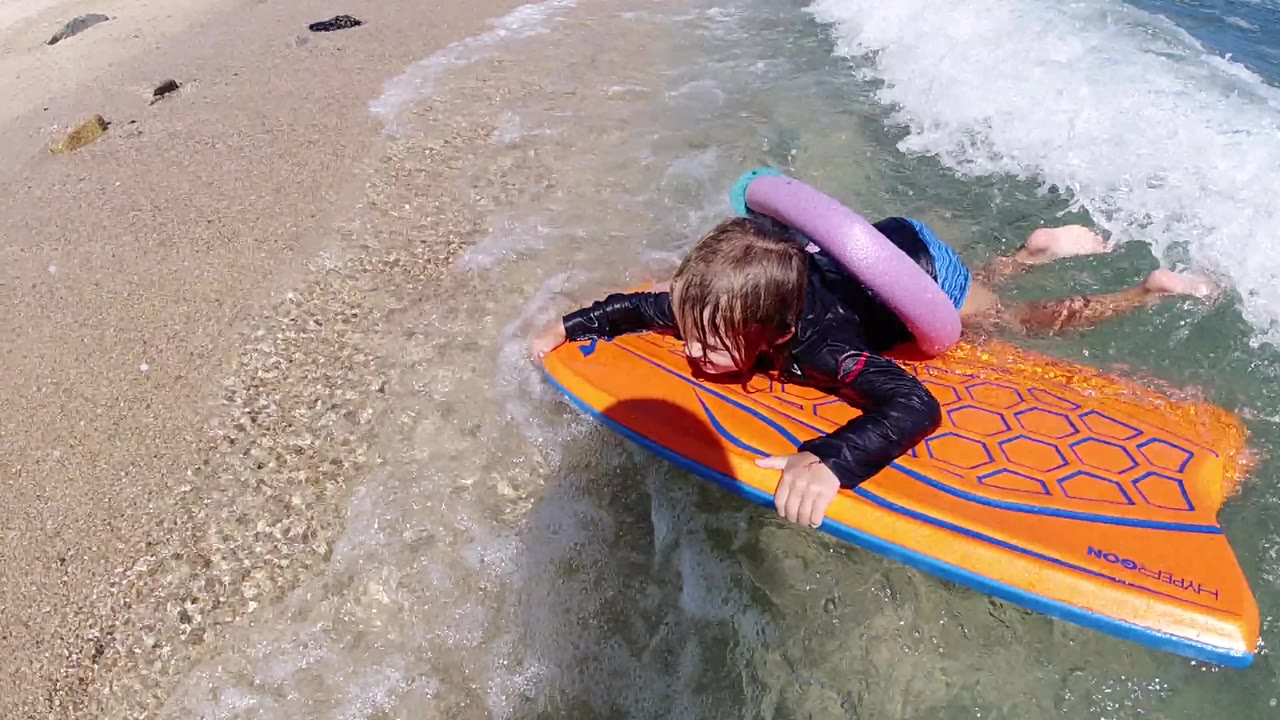 Child holds an orange float at the edge of a small beach wave.