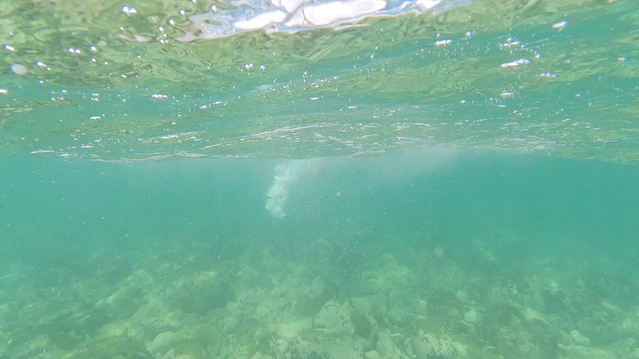 Underwater view in Los Cabos, Mexico with turquoise water, a rippled surface overhead, rocky seabed below, and no visible people.