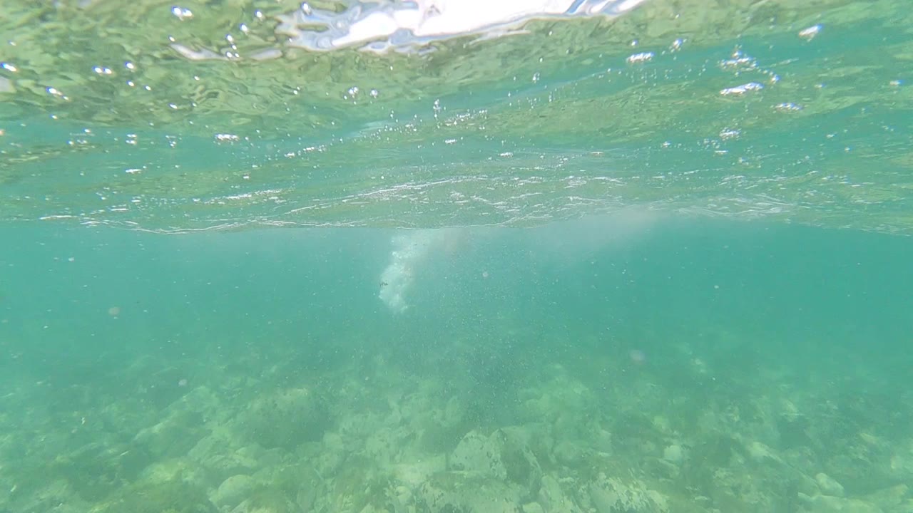 Green-blue underwater frame in Los Cabos, Mexico with surface ripples near the top, pale rocky bottom below, and no visible people.