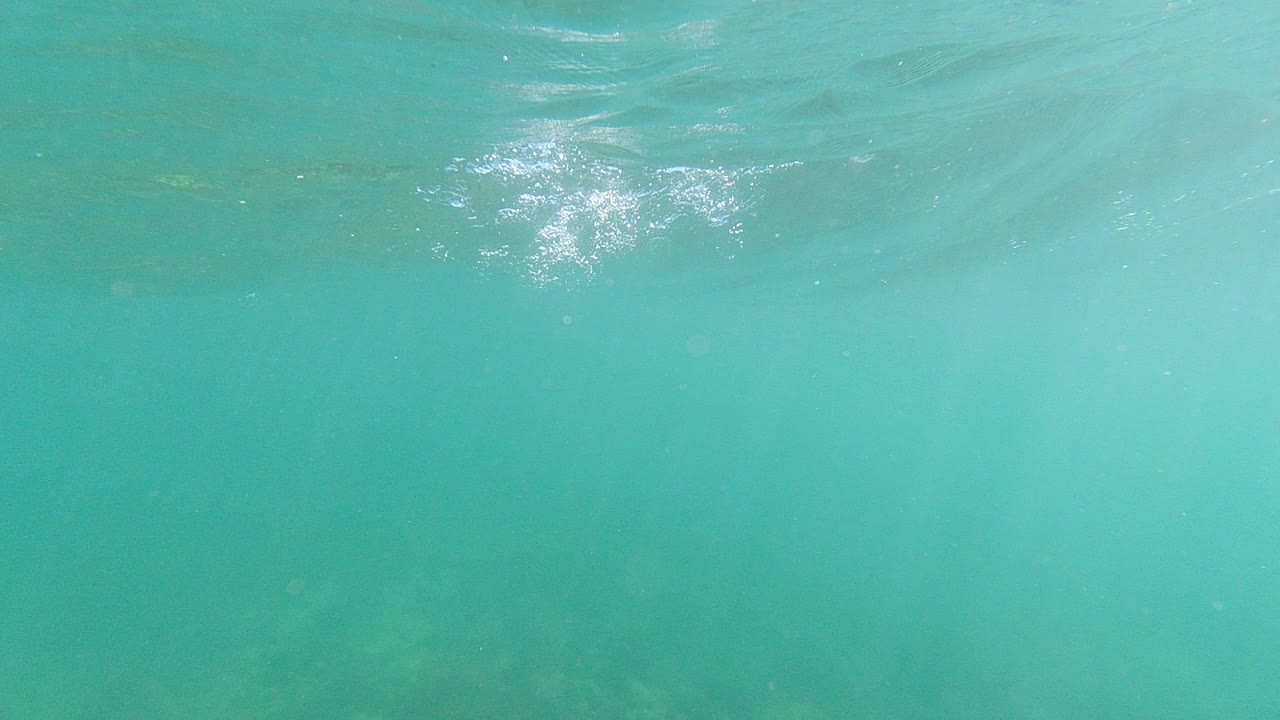 Turquoise underwater view with rippled surface and sun glint.