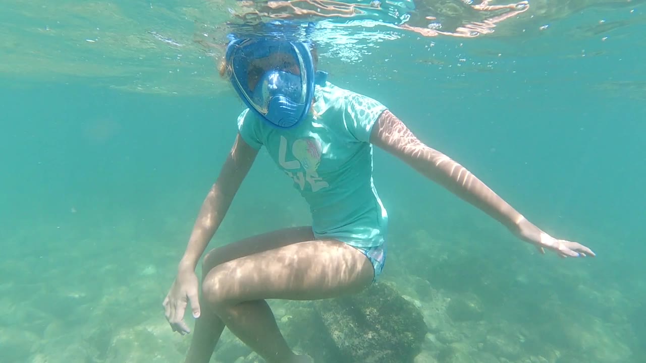 Snorkeler crouches underwater beside pale rocks.