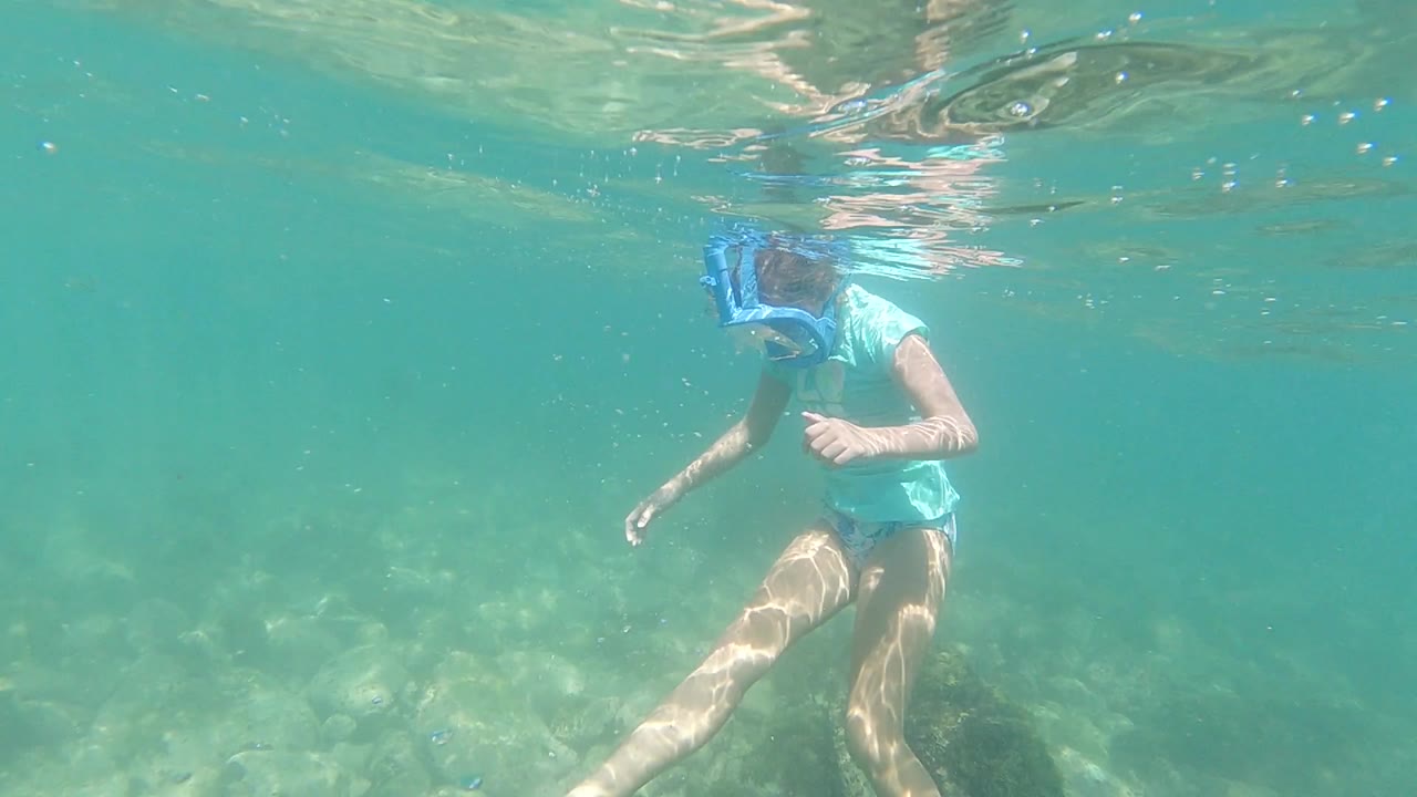 Woman snorkeling underwater near the surface above rocks.