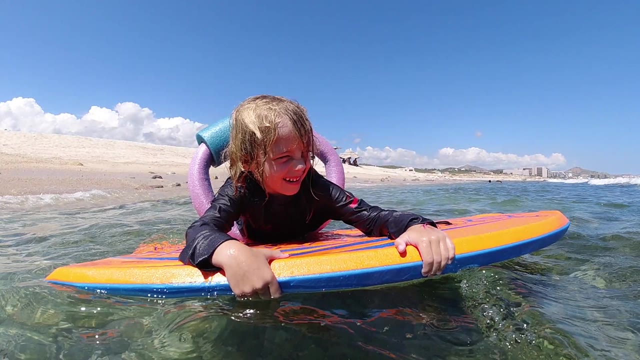 At 0:01, the girl leans forward over the orange bodyboard while small ripples move around the rail in Los Cabos, Mexico.