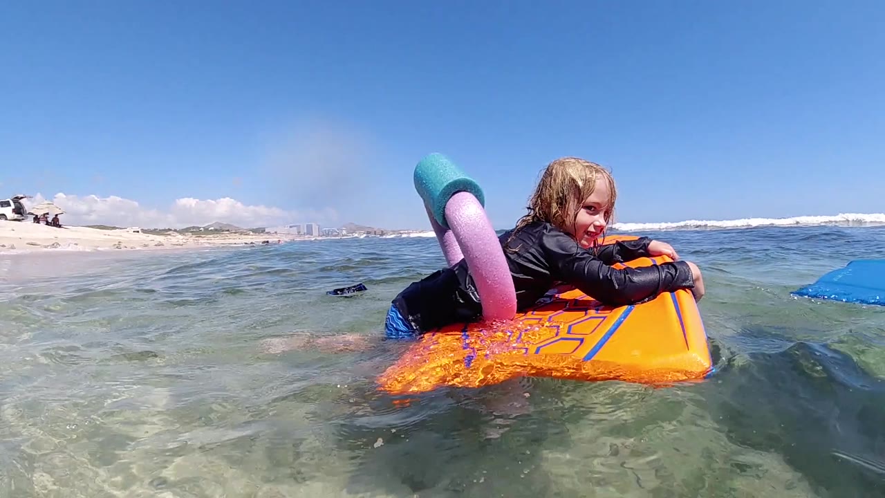 Child gripping orange float in shallow sea.
