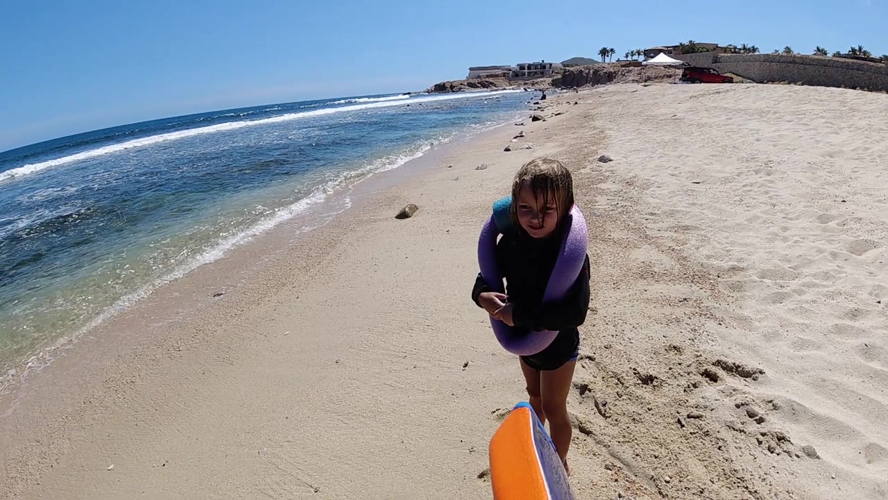 Child standing beside orange float with ocean at left