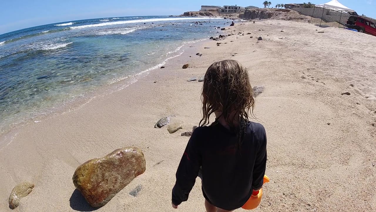 Girl walking down a sandy beach above clear ocean water.