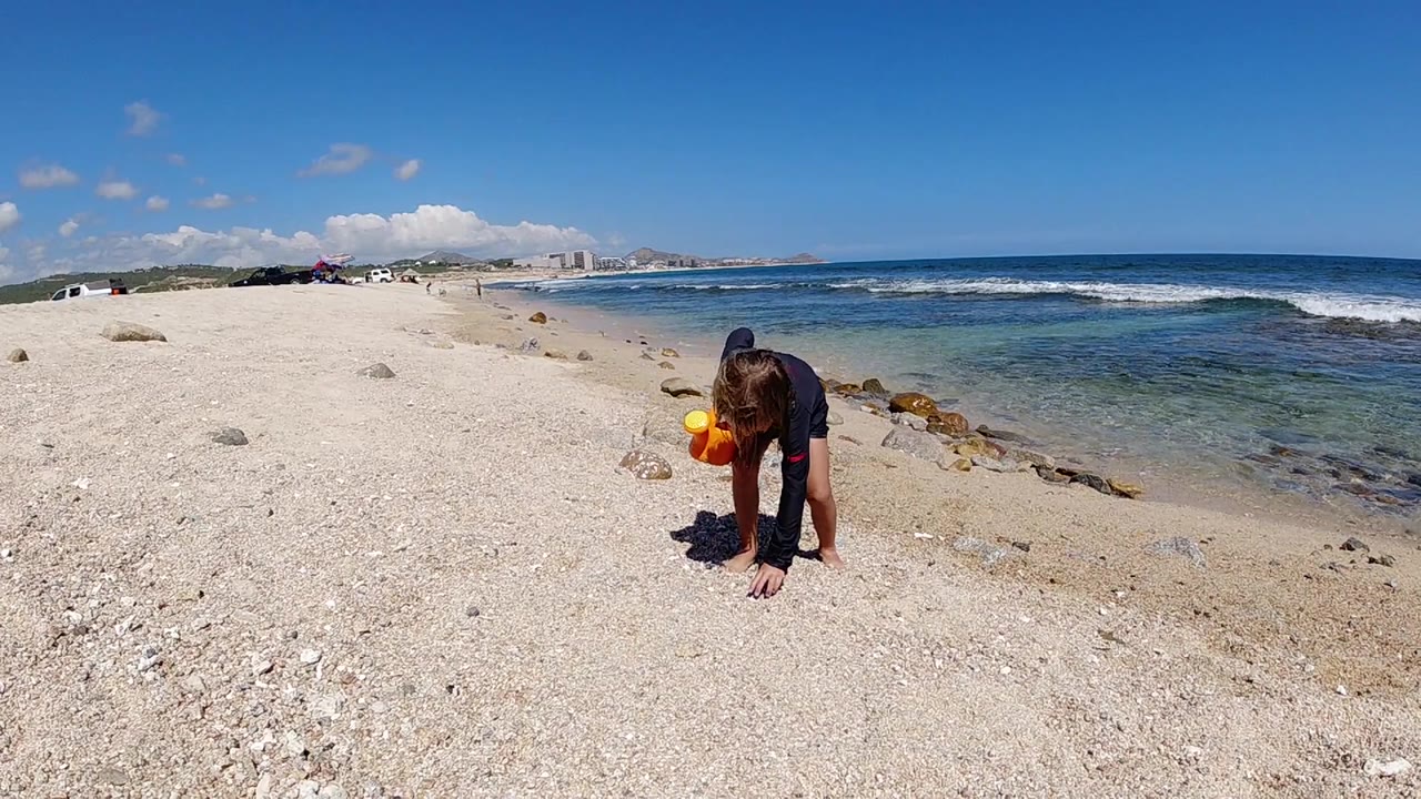 One second in, the girl leans lower over the Los Cabos beach stones as small waves sit farther back in the frame.