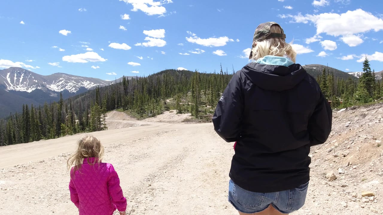 Woman and child continue down a wide dirt road under a blue sky.