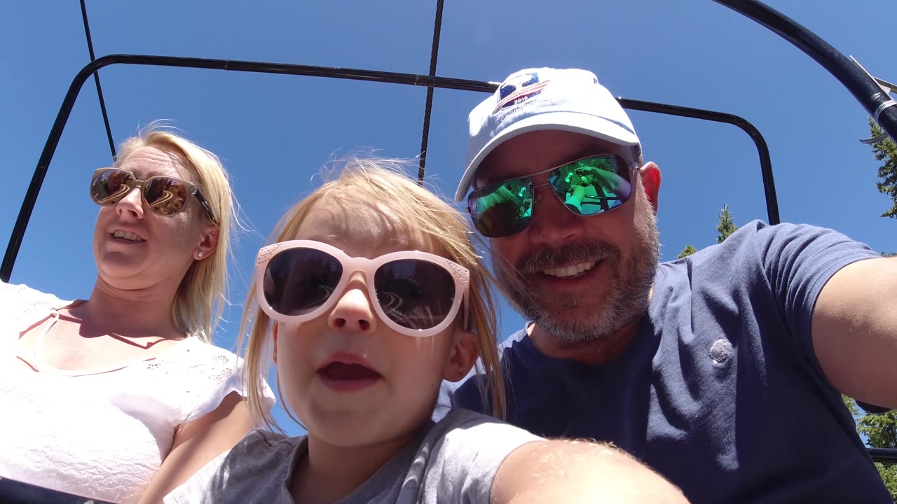 A child in oversized light sunglasses faces the lens while the man beside her smiles and the woman sits slightly farther back.