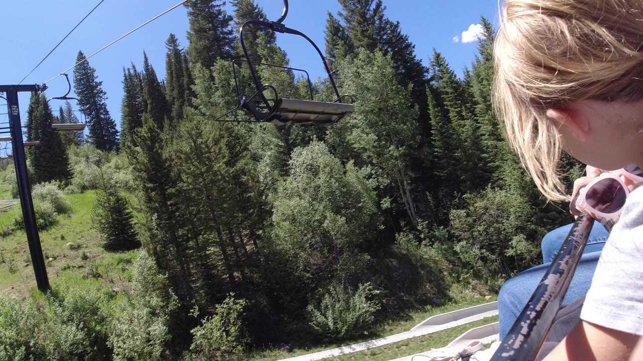 Blonde child on a chairlift above green trees