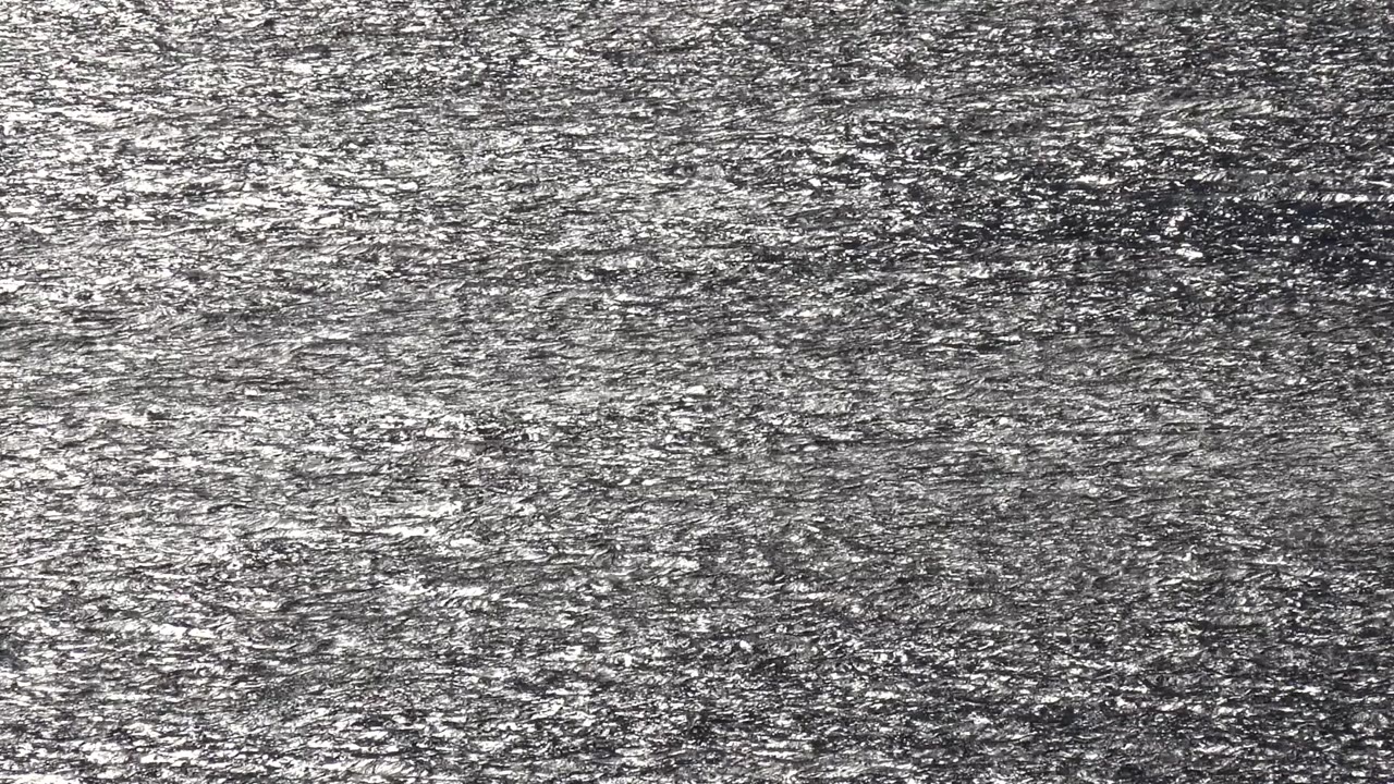 Opening frame of a dark gray shimmering reflective surface in Malibu, California, with dense silver sun highlights and no visible people.