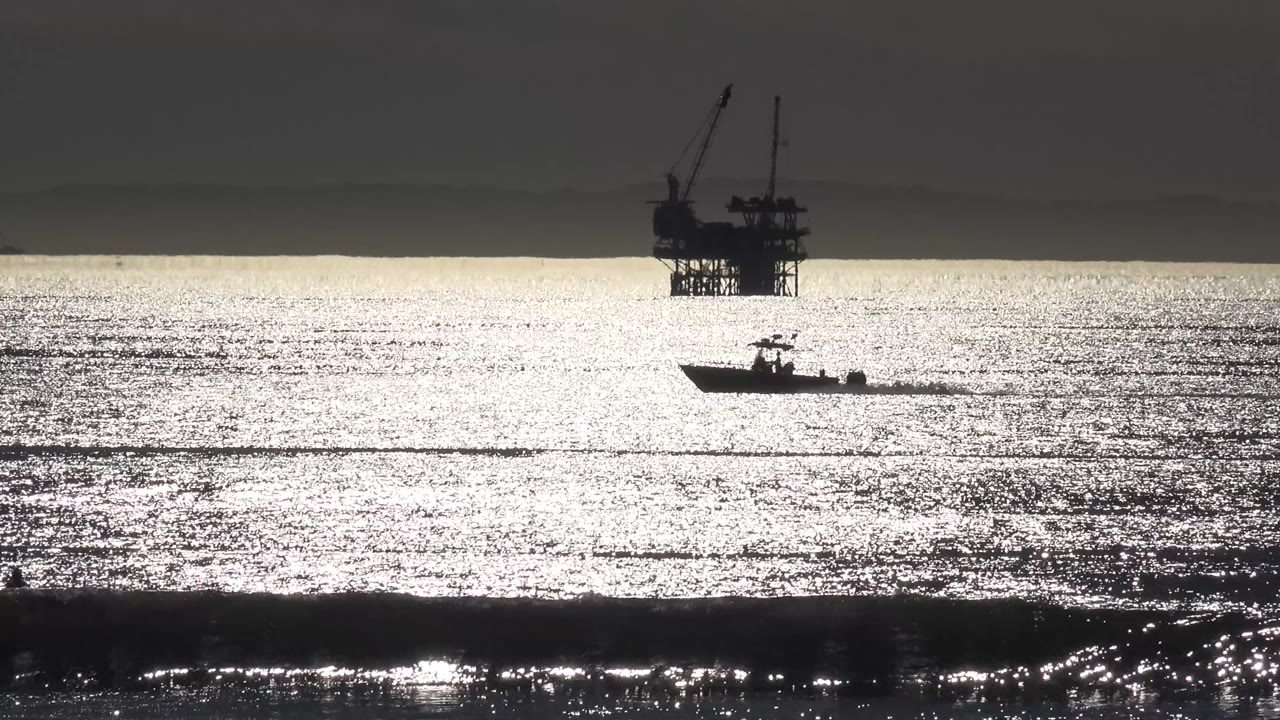 Speed boat on sparkling ocean with an offshore oil rig in the distance.
