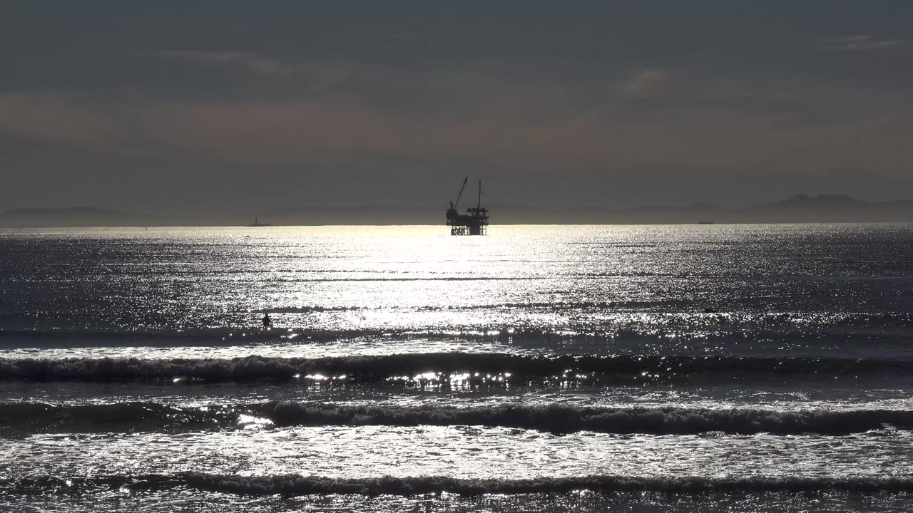 Large offshore boat centered over bright reflective water and low surf lines.