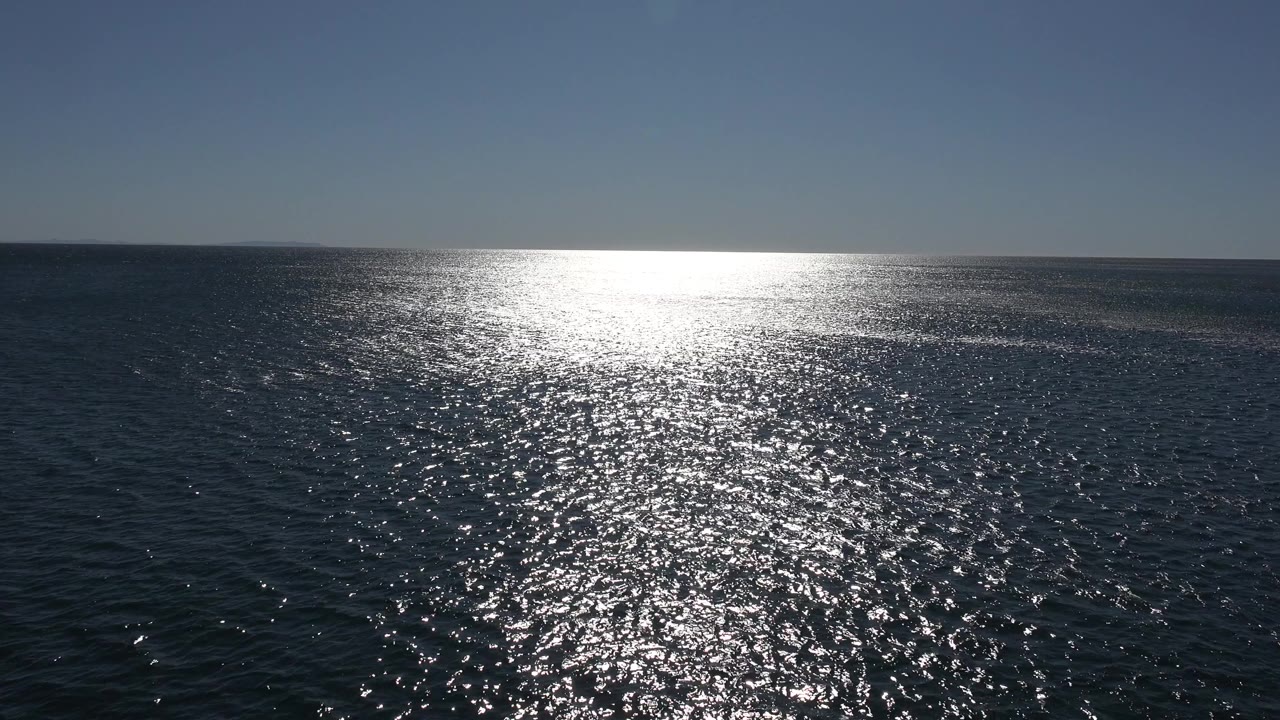 Wide ocean horizon with bright sun reflection on rippled water.