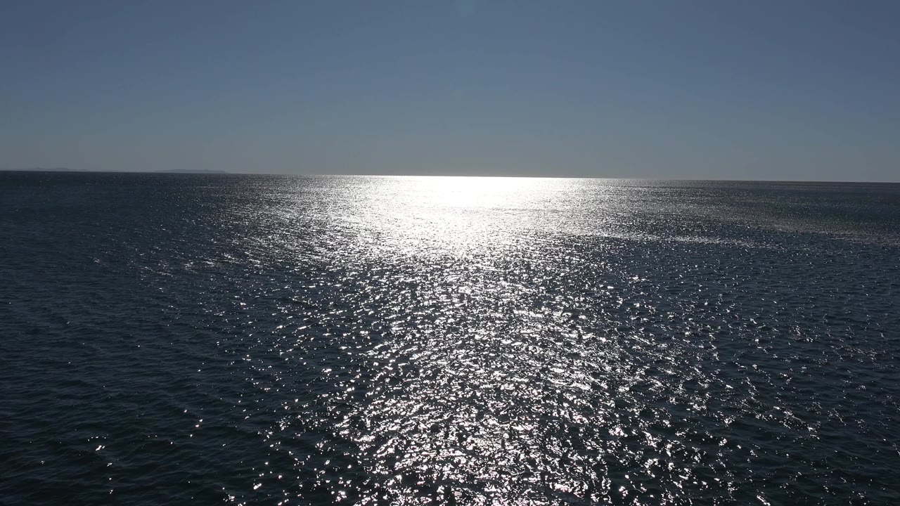 Malibu ocean surface fills the frame as the low sun reflection widens across small waves beneath a clean horizon, with no visible people.