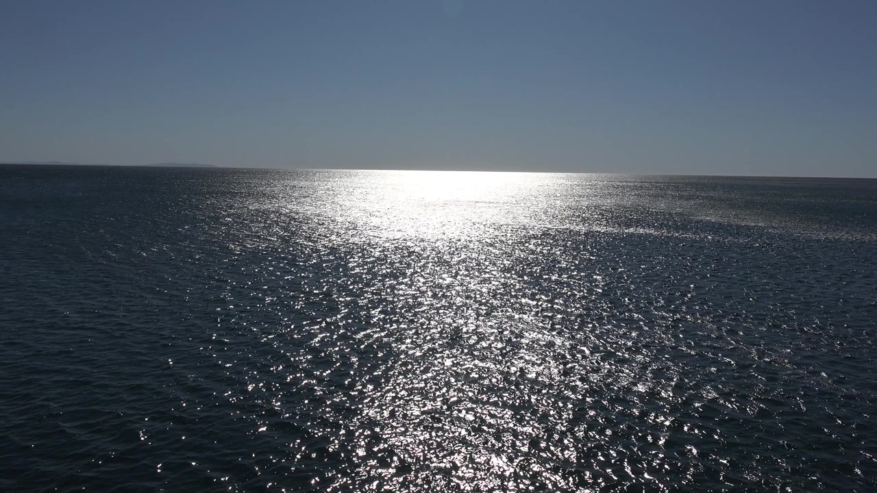 Open Malibu sea and sky hold a centered patch of intense white sunlight on dark water, with no boats, shoreline, or visible people.