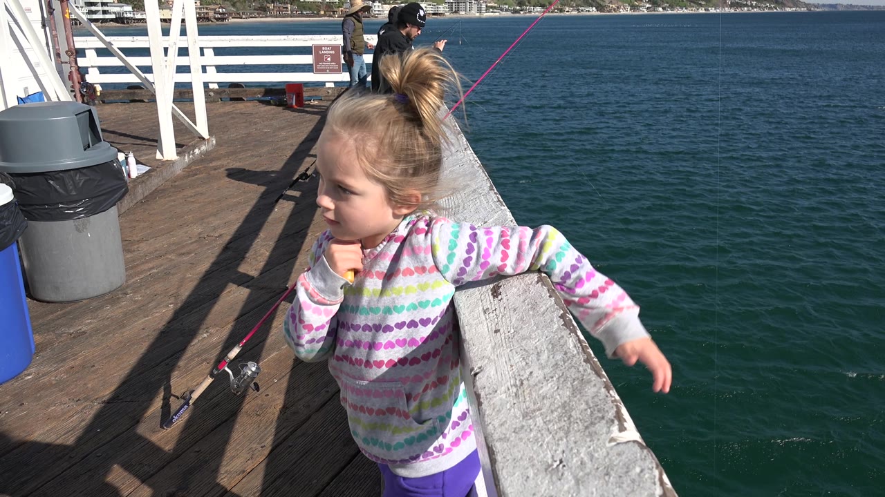 Girl leans sideways on the railing with ocean water behind her.
