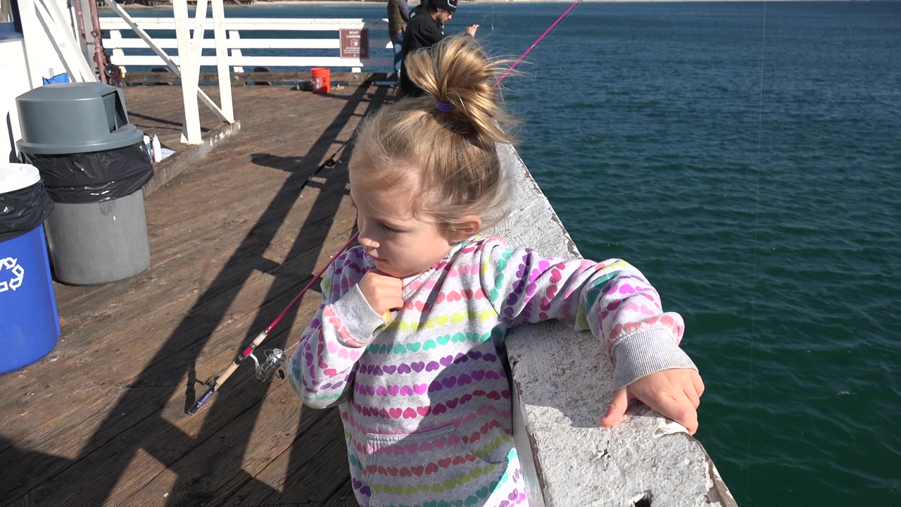 Child leaning against a boat rail near water and deck bins.