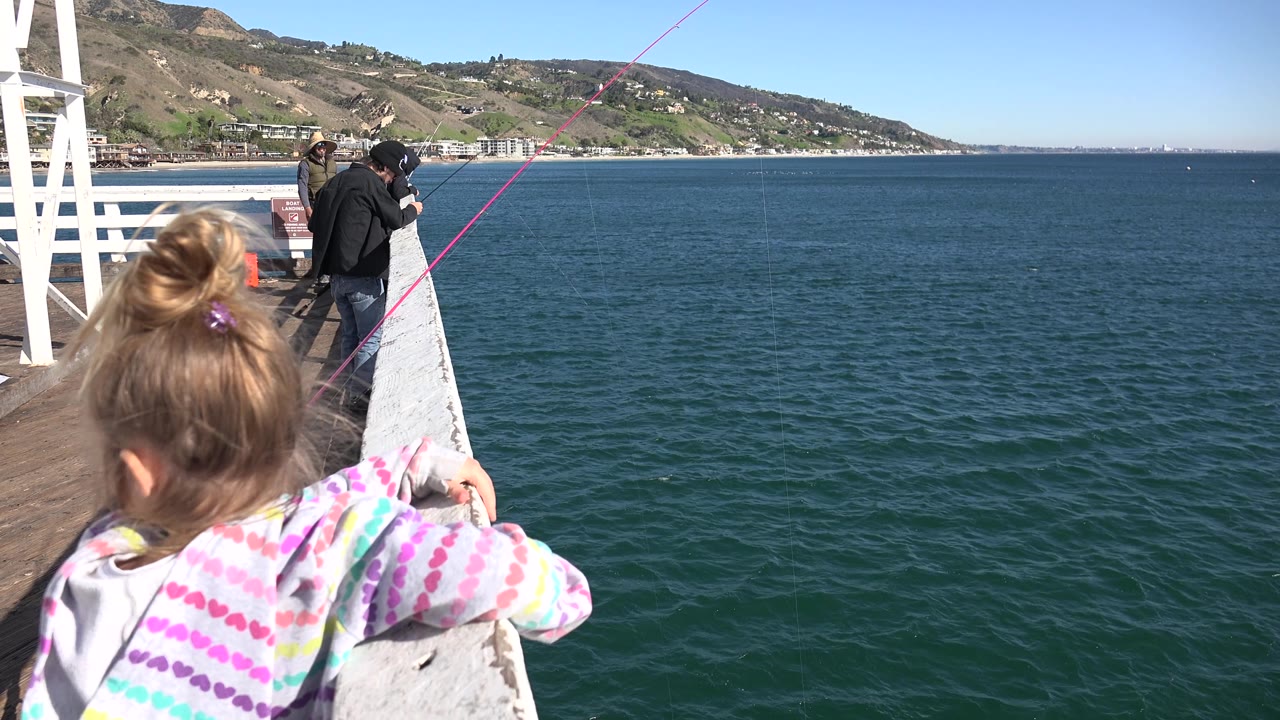 Girl at the pier railing with fishermen farther along the deck.