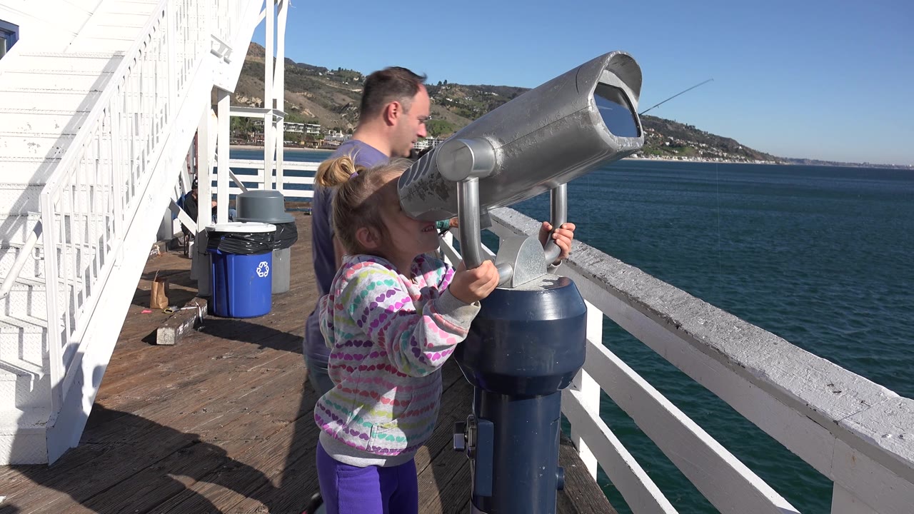 Girl holds the viewer handles while a man stands beside the telescope.