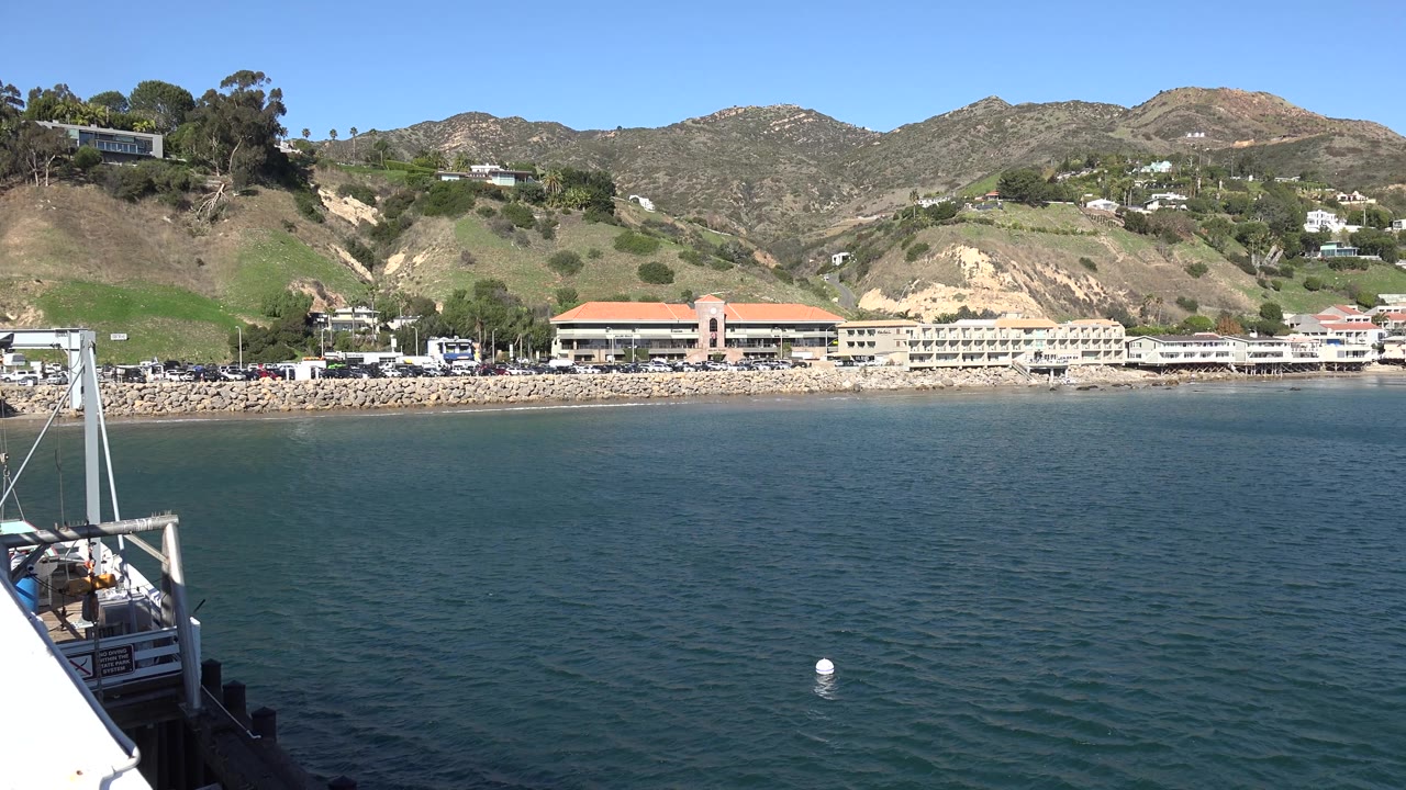 Open water stretches toward Malibu shoreline businesses, tan exposed slopes, green hillside patches, and scattered homes, with no visible people in the frame.