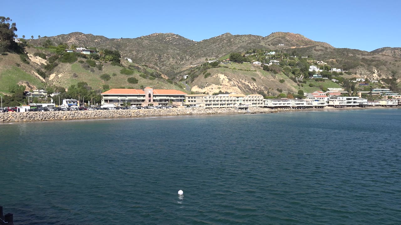 Coastal resort buildings and hills seen over blue water.