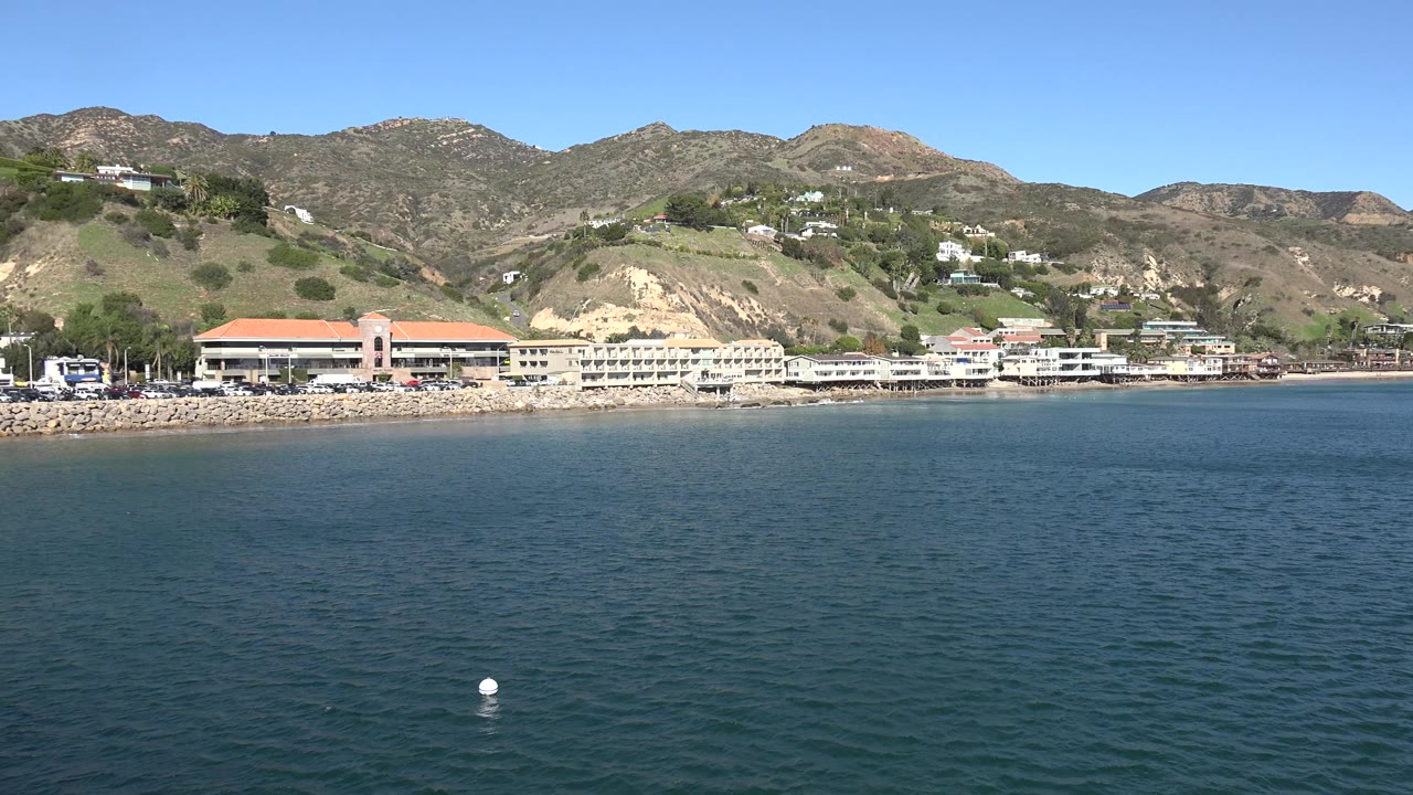Ocean foreground with a white buoy and coastal buildings below hills.