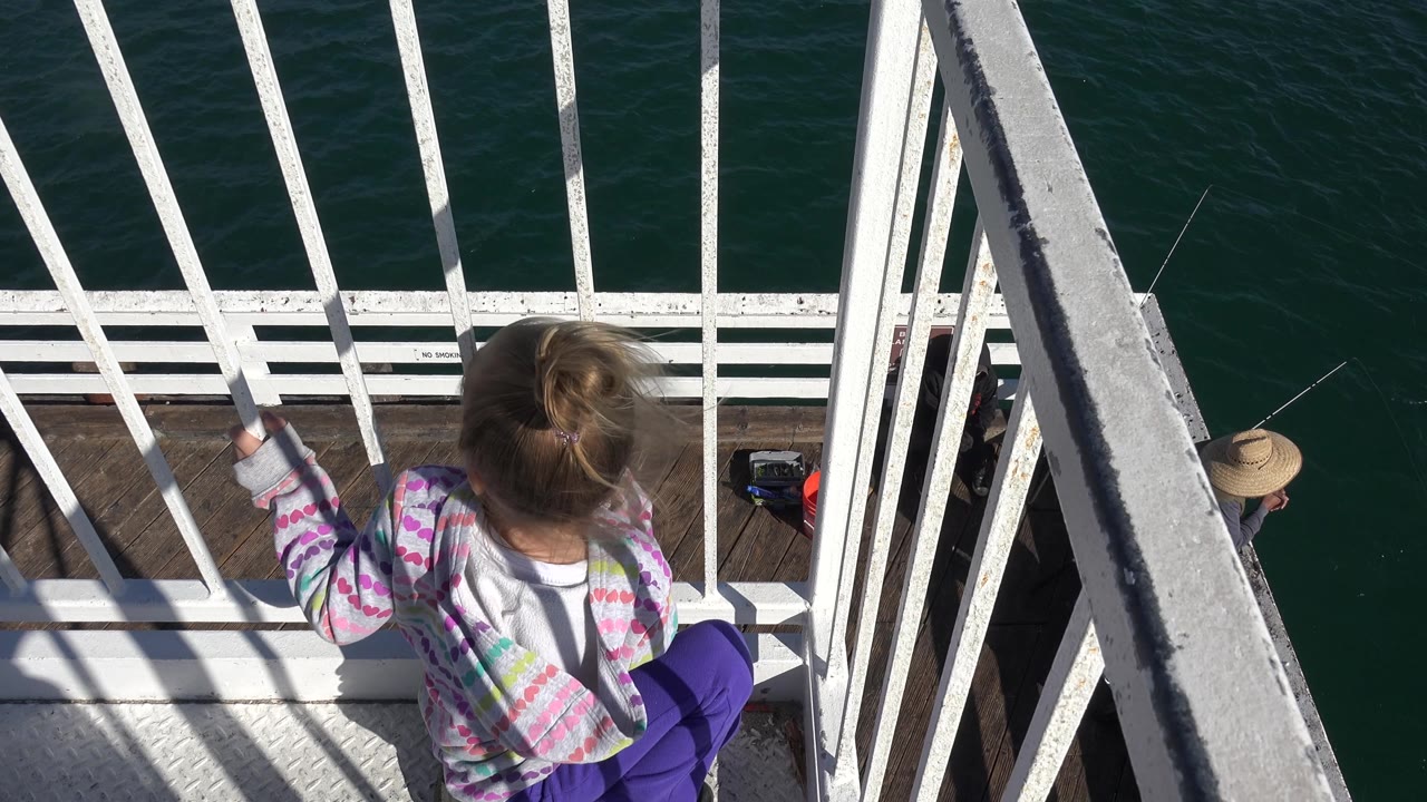 Girl stands at white railings above water with a person partly visible below.